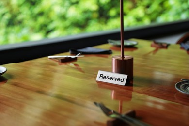 Photo of Sign with word Reserved on wooden table in restaurant