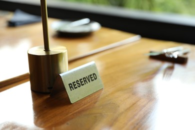 Photo of Sign with word Reserved on wooden table in restaurant, closeup. Space for text