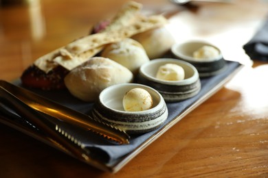 Photo of Tasty buns, crackers and butter served on wooden table, closeup