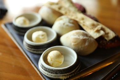 Photo of Tasty buns, crackers and butter served on wooden table, closeup