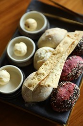 Photo of Tasty buns, crackers and butter served on wooden table, closeup