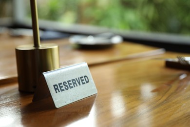 Photo of Sign with word Reserved on wooden table in restaurant, closeup. Space for text