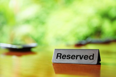 Photo of Sign with word Reserved on wooden table in restaurant, closeup. Space for text