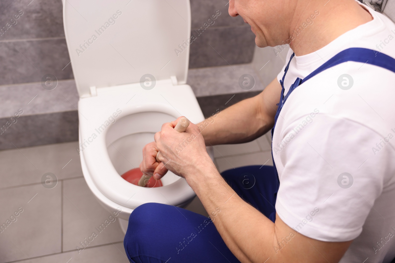 Plumber unclogging toilet with hand plunger indoors, closeup Photo of Plumber unclogging toilet with hand plunger indoors, closeup