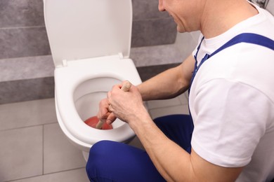Photo of Plumber unclogging toilet with hand plunger indoors, closeup