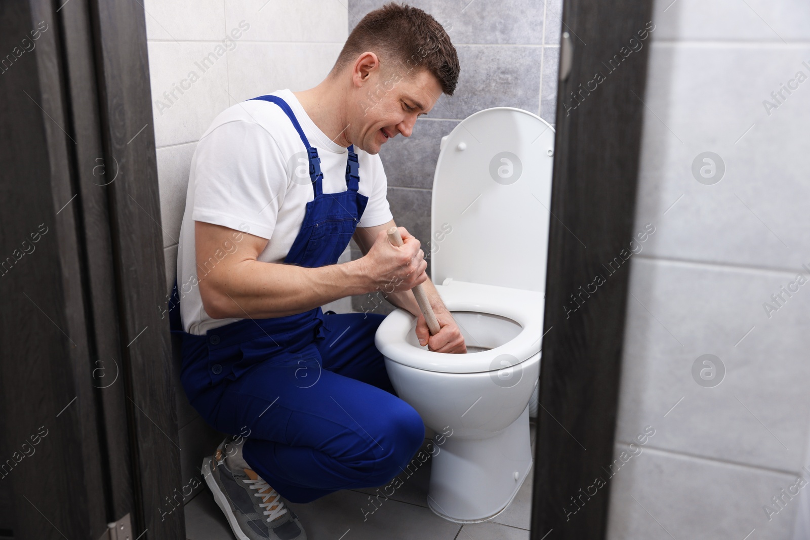 Photo of Plumber unclogging toilet with hand plunger indoors