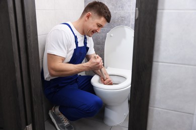 Photo of Plumber unclogging toilet with hand plunger indoors