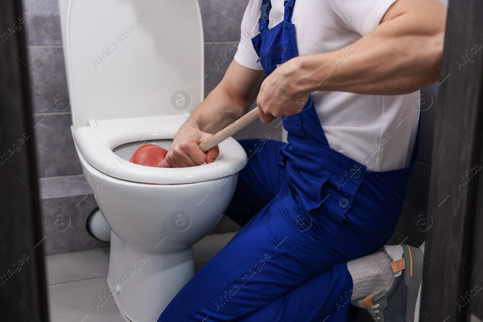 Plumber unclogging toilet with hand plunger indoors, closeup Photo of Plumber unclogging toilet with hand plunger indoors, closeup