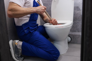 Photo of Plumber unclogging toilet with hand plunger indoors, closeup