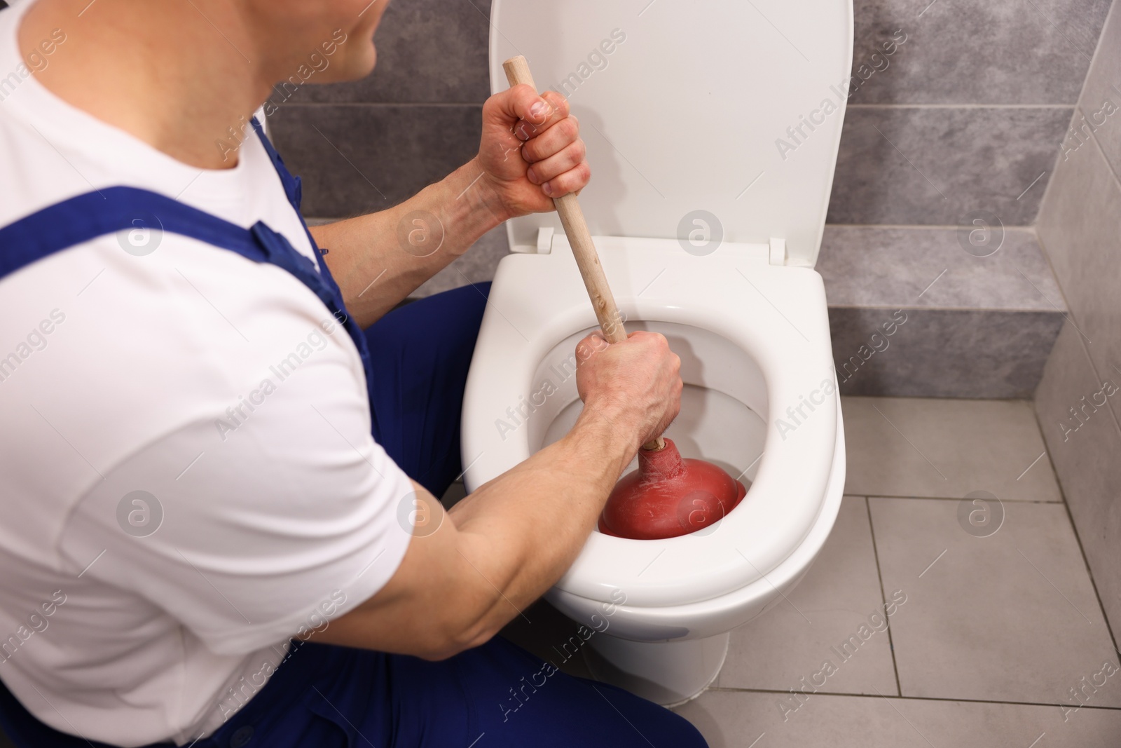 Plumber unclogging toilet with hand plunger indoors, closeup Photo of Plumber unclogging toilet with hand plunger indoors, closeup