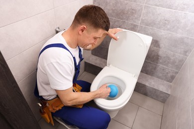 Photo of Plumber unclogging toilet with hand plunger indoors