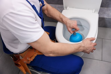 Photo of Plumber unclogging toilet with hand plunger indoors, closeup
