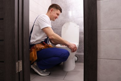 Photo of Plumber unclogging toilet with hand plunger indoors