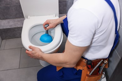 Photo of Plumber unclogging toilet with hand plunger indoors, closeup