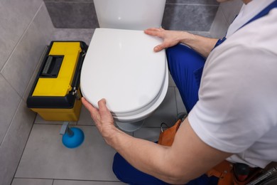 Photo of Professional plumber repairing toilet bowl in restroom, closeup
