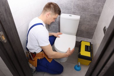 Photo of Professional plumber repairing toilet bowl in restroom