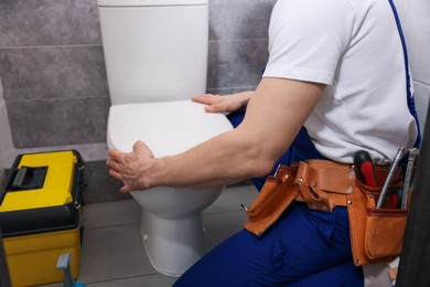 Photo of Professional plumber repairing toilet bowl in restroom, closeup