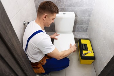 Photo of Professional plumber repairing toilet bowl in restroom
