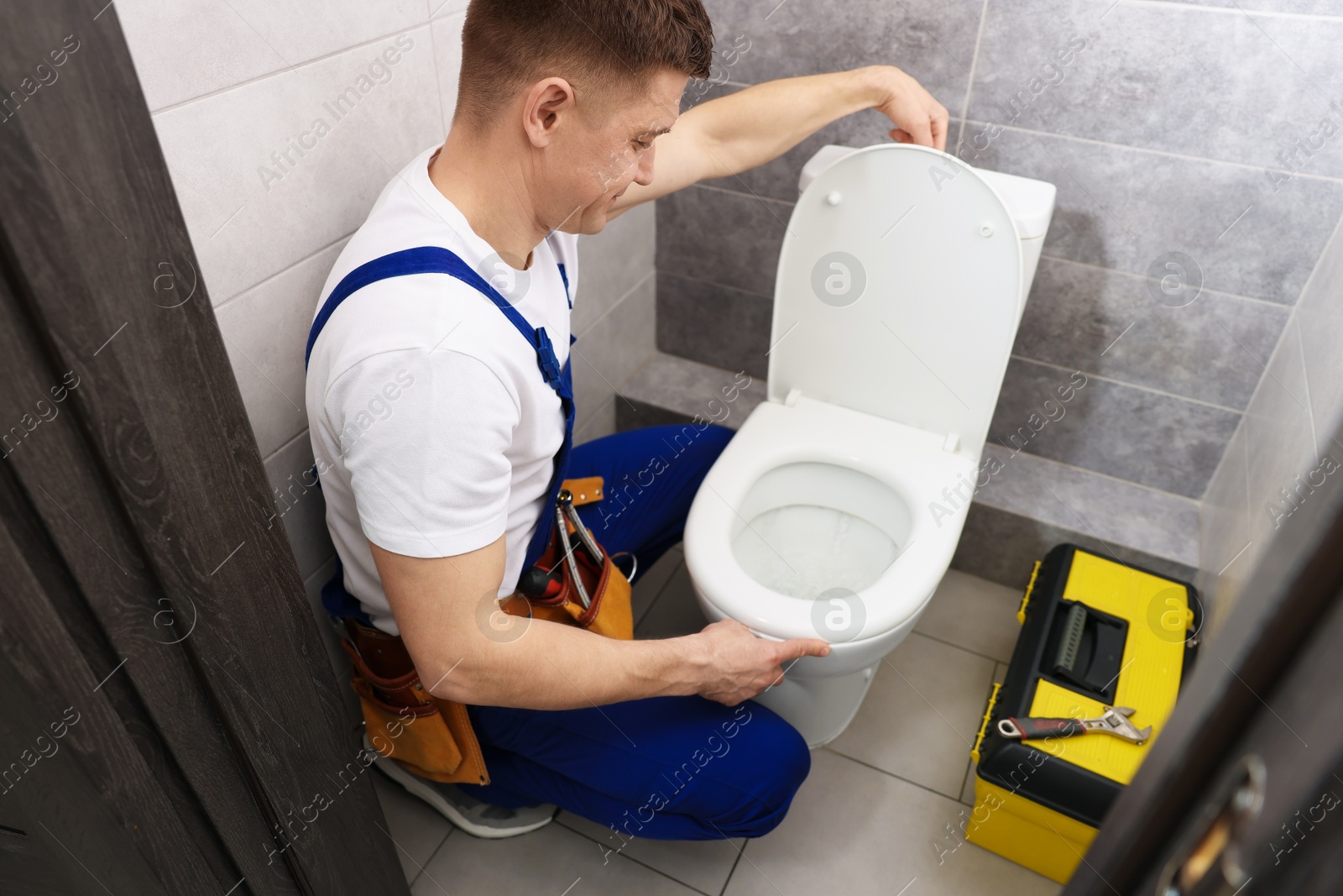 Plumber flushing toilet after repairing it indoors Photo of Plumber flushing toilet after repairing it indoors