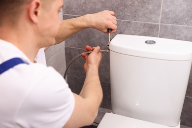 Photo of Professional plumber fixing toilet bowl in restroom, closeup