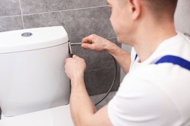 Photo of Professional plumber fixing toilet bowl in restroom, closeup