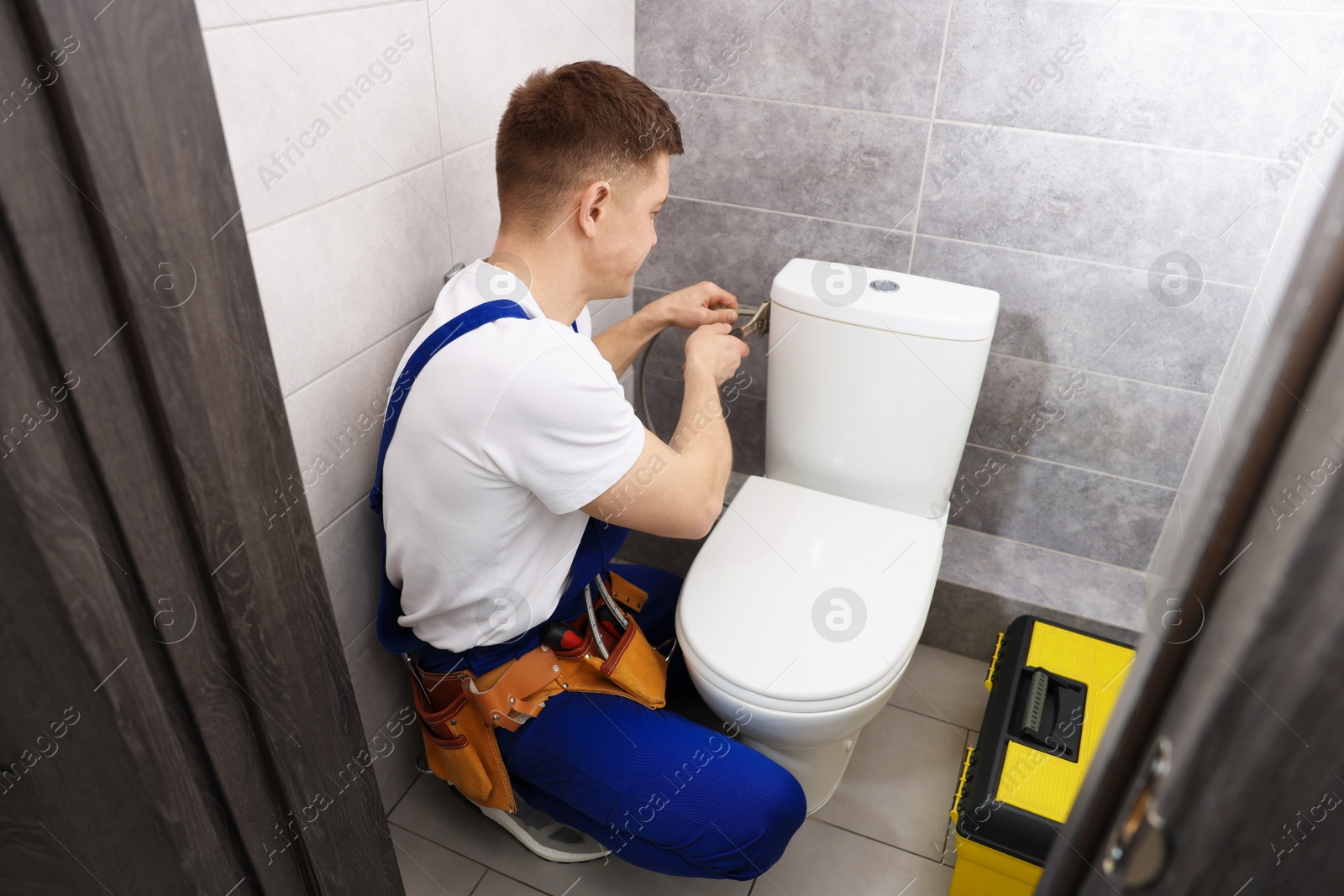 Photo of Professional plumber fixing toilet bowl in restroom