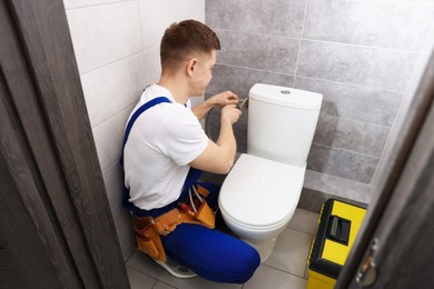 Photo of Professional plumber fixing toilet bowl in restroom