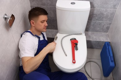 Photo of Professional plumber fixing toilet bowl in restroom