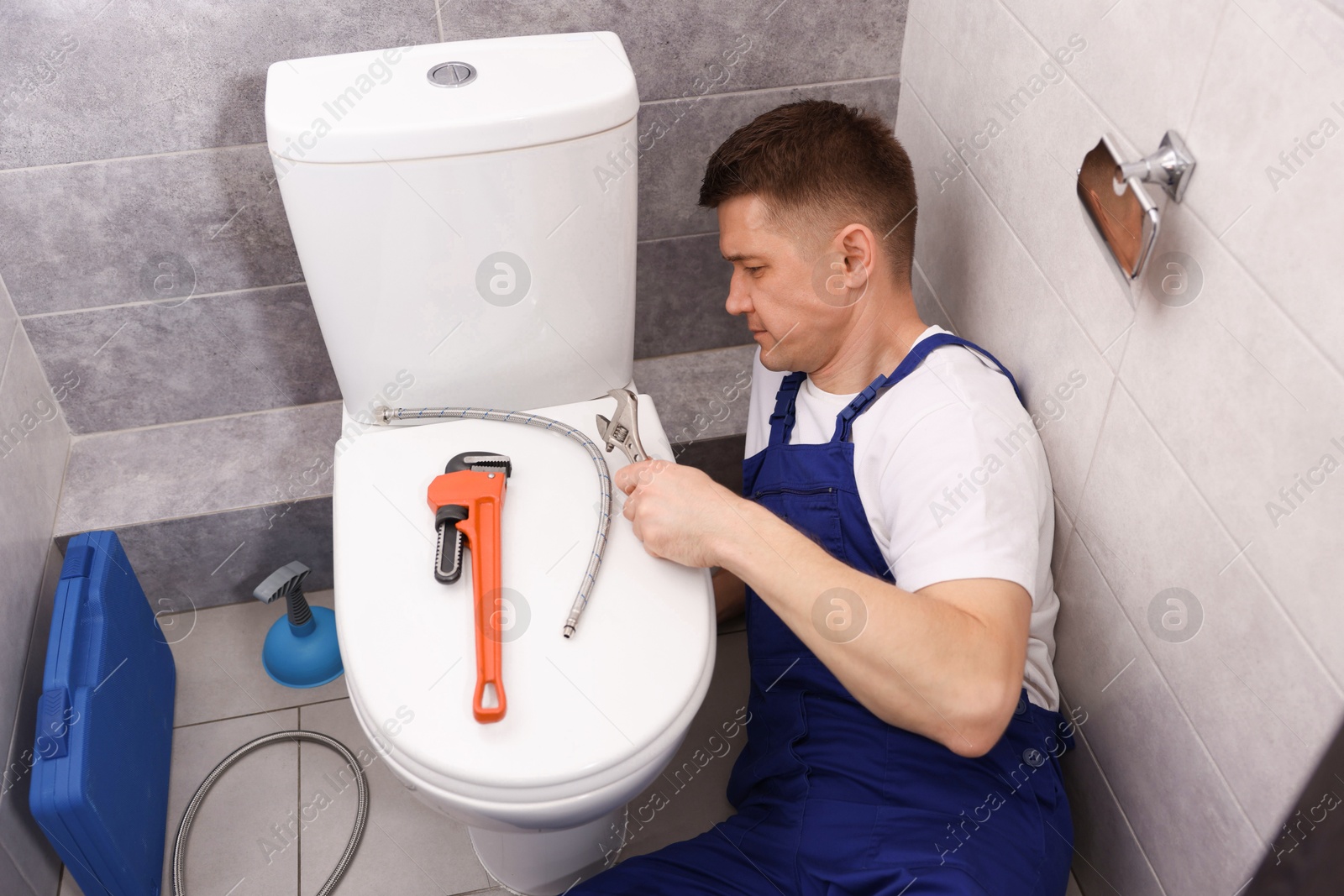 Professional plumber fixing toilet bowl in restroom Photo of Professional plumber fixing toilet bowl in restroom