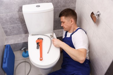 Photo of Professional plumber fixing toilet bowl in restroom