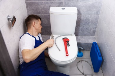 Photo of Professional plumber fixing toilet bowl in restroom