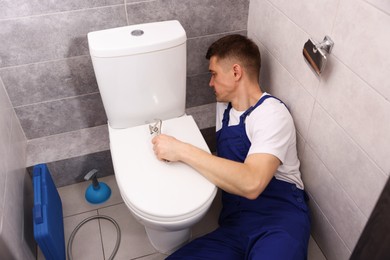 Photo of Professional plumber fixing toilet bowl in restroom