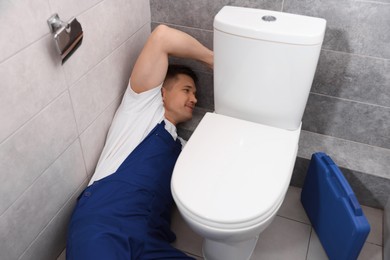 Photo of Professional plumber fixing toilet bowl in restroom