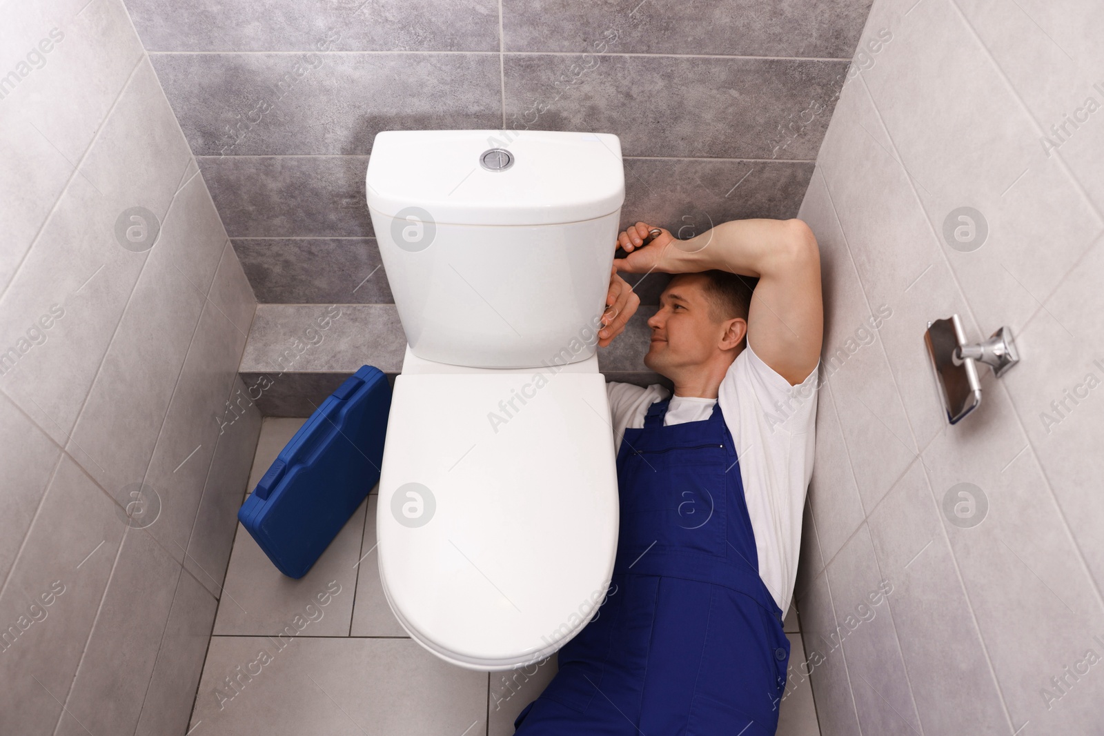 Professional plumber fixing toilet bowl in restroom, above view Photo of Professional plumber fixing toilet bowl in restroom, above view