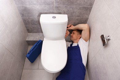 Photo of Professional plumber fixing toilet bowl in restroom, above view