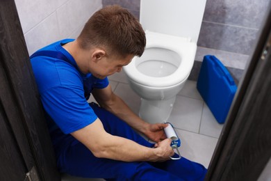 Photo of Professional plumber sealing toilet bowl in restroom