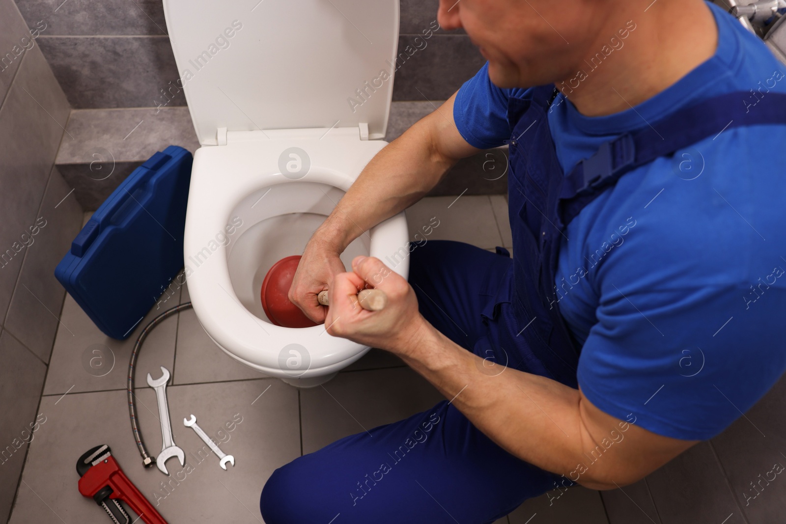 Plumber unclogging toilet with hand plunger indoors, closeup Photo of Plumber unclogging toilet with hand plunger indoors, closeup