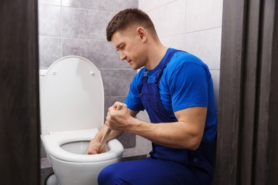 Photo of Plumber unclogging toilet with hand plunger indoors