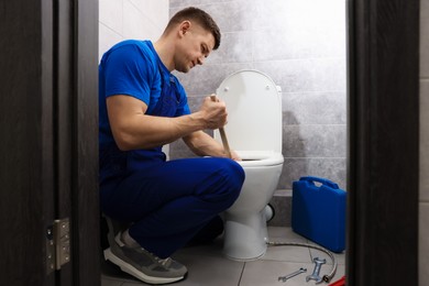 Photo of Plumber unclogging toilet with hand plunger indoors