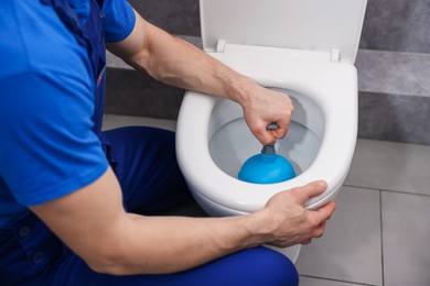 Photo of Plumber unclogging toilet with hand plunger indoors, closeup