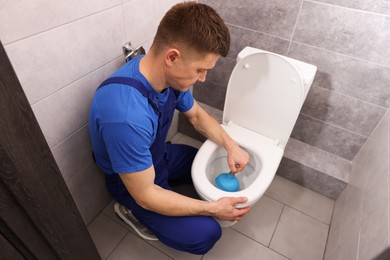 Photo of Plumber unclogging toilet with hand plunger indoors, above view