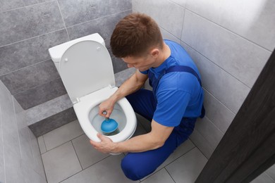 Photo of Plumber unclogging toilet with hand plunger indoors, above view