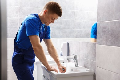 Photo of Plumber unclogging sink with hand plunger indoors