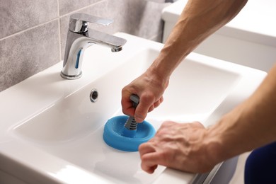 Photo of Plumber unclogging sink with hand plunger indoors, closeup