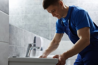 Photo of Plumber unclogging sink with hand plunger indoors