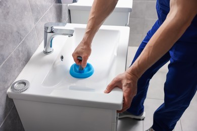 Photo of Plumber unclogging sink with hand plunger indoors, closeup