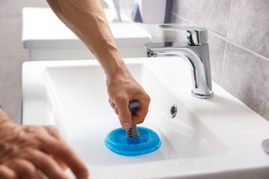 Photo of Plumber unclogging sink with hand plunger indoors, closeup