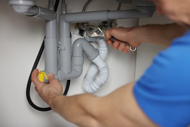 Photo of Plumber fixing pipes under sink indoors, closeup