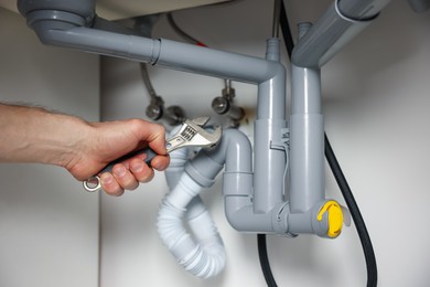 Photo of Plumber fixing pipes under sink indoors, closeup