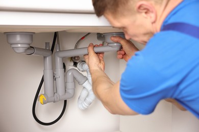 Photo of Plumber fixing pipes under sink indoors, closeup
